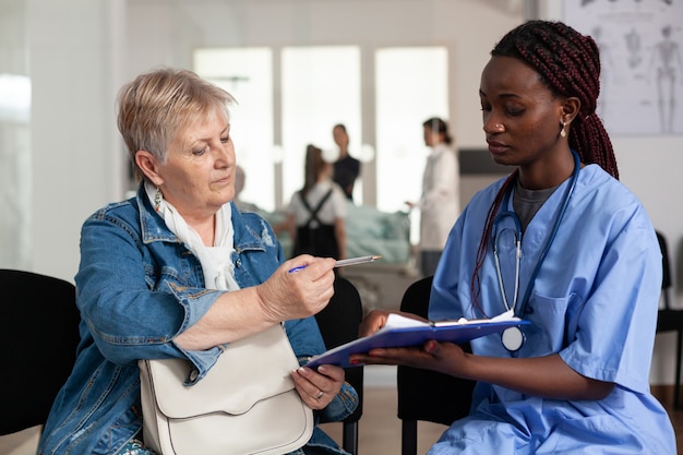 Enfermera afroamericana explicando el tratamiento de la enfermedad al paciente anciano