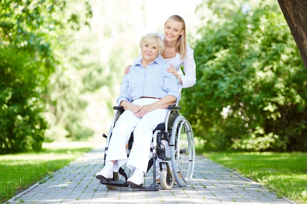 Enfermera caminando con la paciente mayor en silla de ruedas