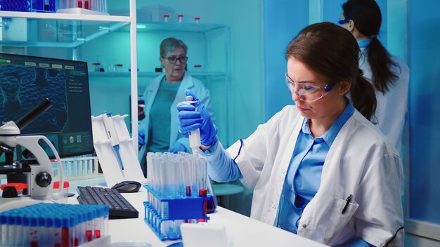 Enfermera científica con micropipeta para llenar tubos de ensayo en un laboratorio equipado moderno trabajando horas extraordinarias