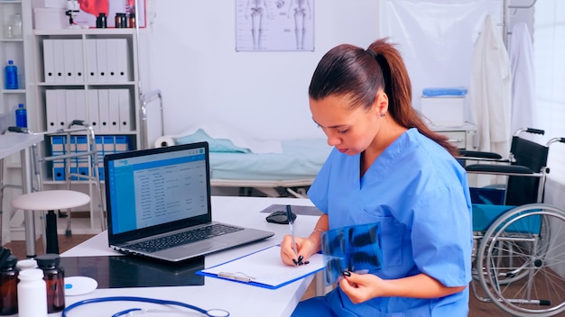 Enfermera comprobando el resultado de la radiografía, leyendo la lista de pacientes, tomando notas en el portapapeles con radiografía. Médico en medicina uniforme escribiendo una lista de pacientes consultados y diagnosticados, realizando una investigación.