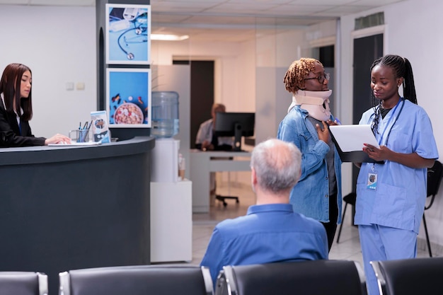 Enfermera consultando a una mujer con cuello ortopédico, brindando asistencia médica para curar lesiones. Especialista y paciente hablando sobre seguro médico y tratamiento en el área de la sala de espera, adulto lesionado.