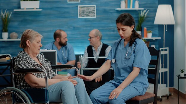 Enfermera consultando a una mujer jubilada sentada en silla de ruedas en una clínica de enfermería. Asistente médico que realiza un chequeo médico con un paciente anciano discapacitado para recibir tratamiento y recuperación del dolor.