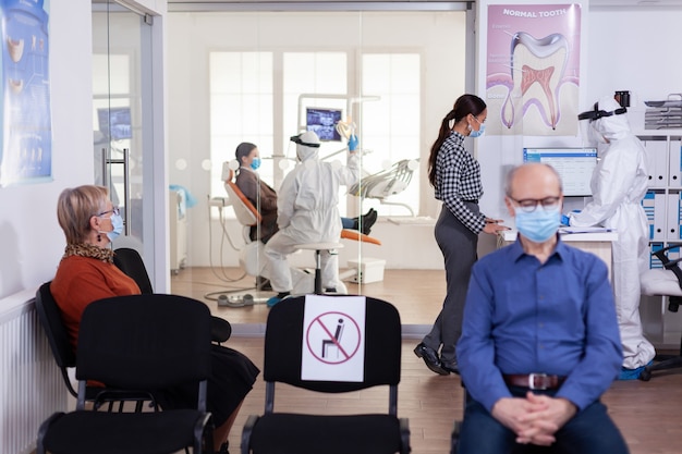 Enfermera dentista vestida con traje de ppe con rostro shiled discutiendo con el paciente en la sala de espera de estomatología