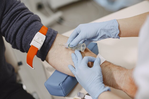 La enfermera experta está haciendo análisis de sangre para el hombre en la clínica. Hombre con una máscara médica.