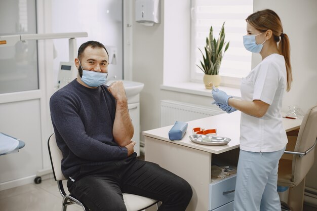 La enfermera experta está haciendo análisis de sangre para el hombre en la clínica. Hombre con una máscara médica.