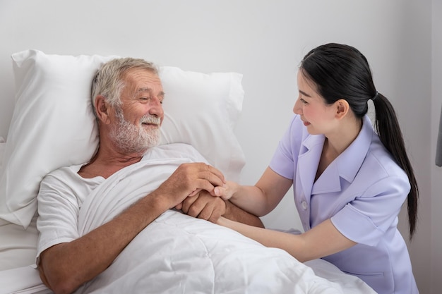 Enfermera feliz sosteniendo las manos de un anciano con una manta en el dormitorio en el hogar de ancianos