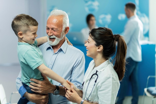 Enfermera feliz tomándose de la mano y comunicándose con un niño pequeño que vino con su abuelo a la clínica El foco está en el abuelo
