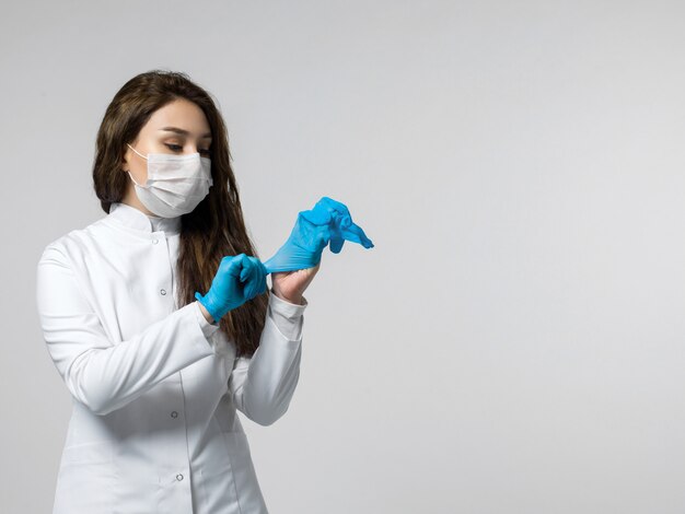 Enfermera con guantes azules, uniforme médico blanco y máscara médica estéril protectora blanca