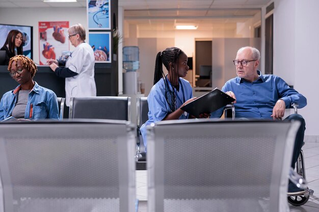 Enfermera hablando con un paciente anciano con discapacidad crónica, sentada en silla de ruedas en la sala de espera. Asistente médico consultando a un hombre con discapacidad física, dando tratamiento para la recuperación.