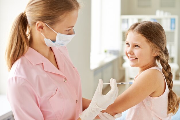 Enfermera inyectando a una niña sonriente
