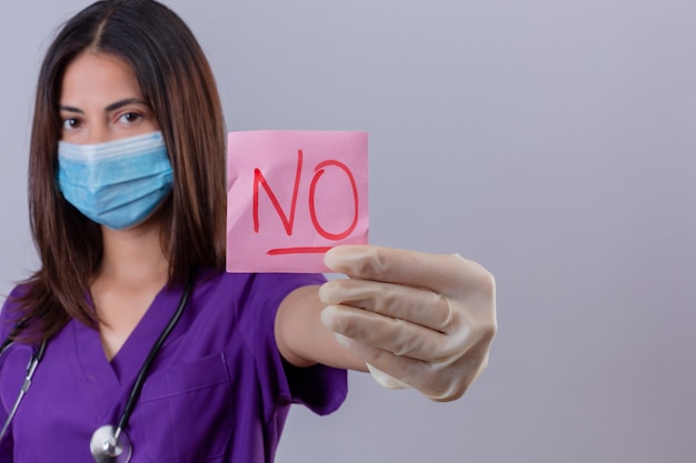 Foto gratuita enfermera joven con guantes de máscara protectora uniforme médico y con estetoscopio mostrando papel recordatorio con la palabra no parece seguro