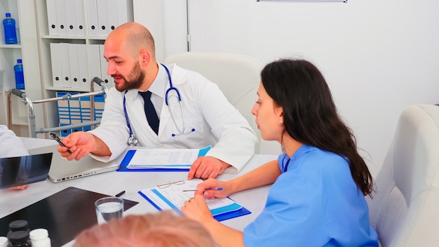 Enfermera médica hablando con médicos, informando con expertos en medicina en la sala de conferencias del hospital. Terapeuta clínico con colegas hablando de enfermedad, experto, especialista, comunicación.