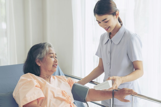 Enfermera que mide la presión arterial de una anciana mayor en pacientes en cama de hospital - concepto senior médico y sanitario