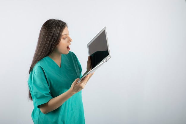 Foto gratuita enfermera de sexo femenino joven que mira la computadora portátil en blanco.