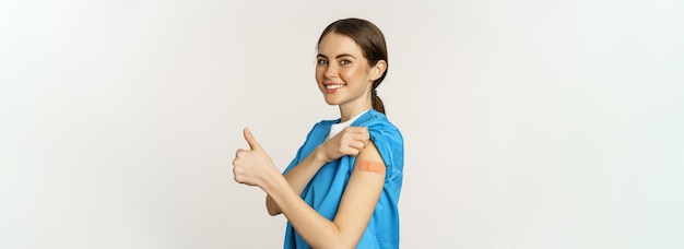 Foto gratuita enfermera sonriente doctor en matorrales trabajador médico mostrando su hombro vacunado con parche thumbs up r