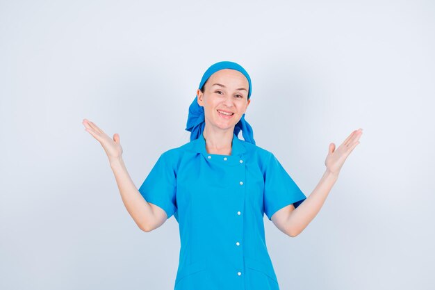 Enfermera sonriente está mirando a la cámara abriendo sus manos sobre fondo blanco.