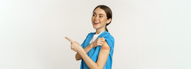 Foto gratuita enfermera sonriente trabajadora de la salud en matorrales apuntando con el dedo a la derecha mostrando el parche en la aspiradora del hombro