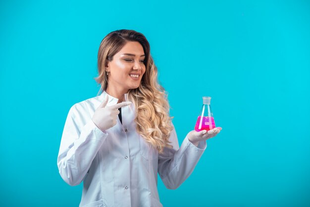 Enfermera en uniforme blanco sosteniendo un matraz químico con líquido rosa y puntos.