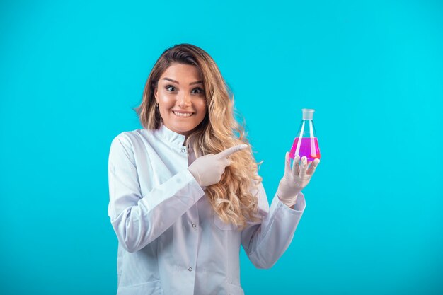 Enfermera en uniforme blanco sosteniendo un matraz químico con líquido rosa y se siente exitosa.