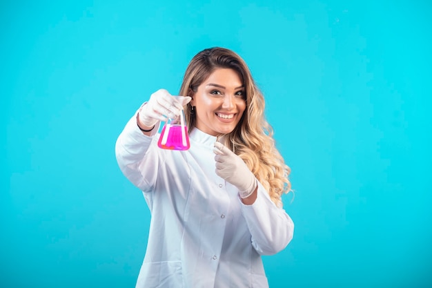 Enfermera en uniforme blanco sosteniendo un matraz químico con líquido rosa y se siente positiva.