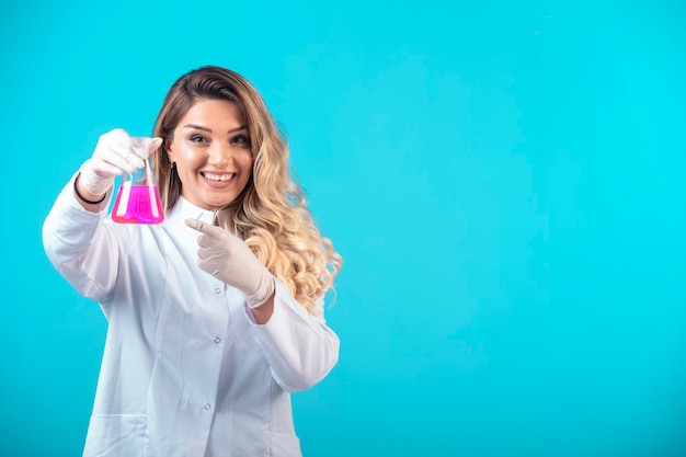 Enfermera en uniforme blanco sosteniendo un matraz químico con líquido rosa y se siente positiva.