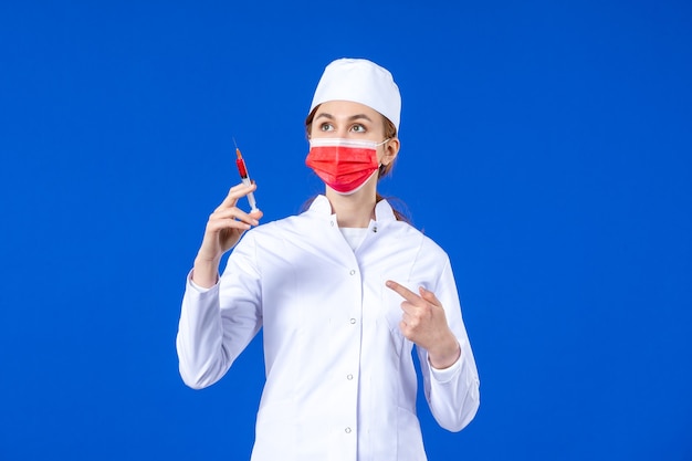 Enfermera de vista frontal en traje médico blanco con máscara roja e inyección en sus manos en azul