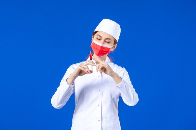 Enfermera de vista frontal en traje médico blanco con máscara roja e inyección en sus manos en azul