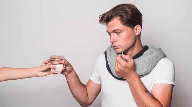 Enfermo sosteniendo la cápsula tomando un vaso de agua de la mano de la persona