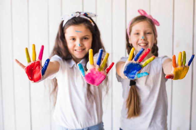 Foto gratuita enfoque selectivo de dos chicas sonrientes mostrando pintura colorida manos