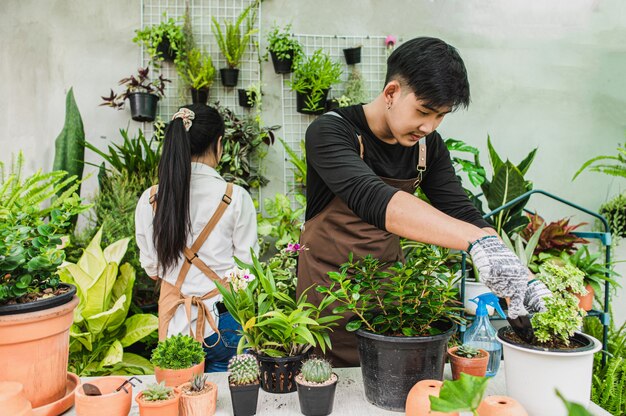 Enfoque selectivo, el hombre joven usa el trasplante de pala y cuida la planta de la casa, la mujer que trabaja detrás de él