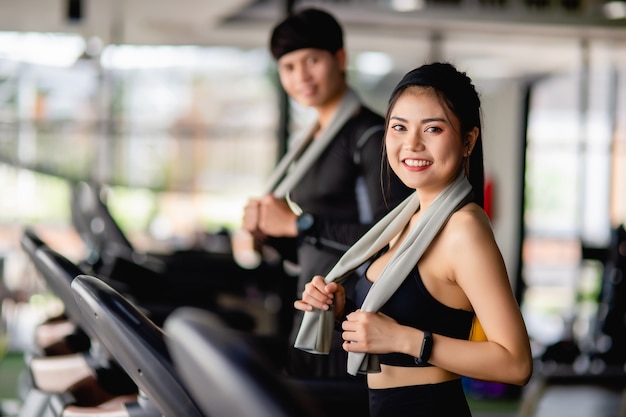 Enfoque selectivo, retrato de mujer sexy en ropa deportiva, corriendo en la cinta de correr, hombre guapo borroso correr casi, están haciendo ejercicio en el moderno gimnasio, sonrisa, espacio de copia