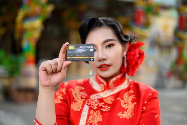 Enfoque selectivo, tarjeta de crédito en la mano de una bella mujer asiática que lleva un cheongsam sonriendo y posa en el santuario en el año nuevo chino