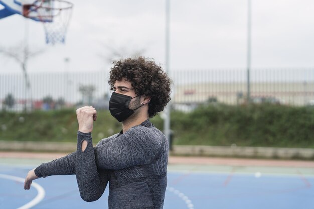Enfoque superficial de un atleta masculino de pelo rizado con una máscara facial trabajando en una cancha de baloncesto