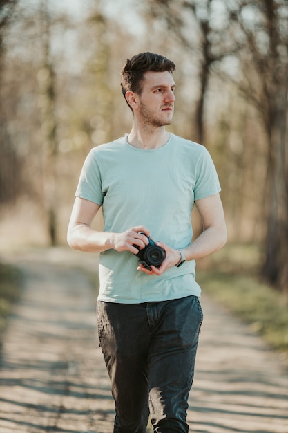 Enfoque superficial de un fotógrafo macho adulto sosteniendo una cámara y caminando por un parque