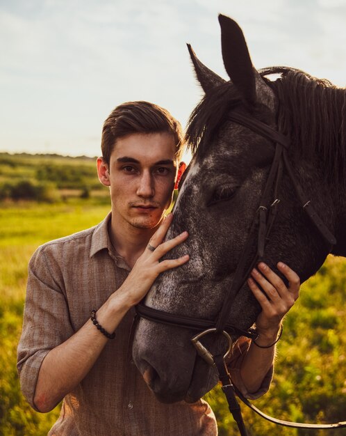 Enfoque superficial de un joven macho acariciando un caballo en un campo bajo la luz del sol