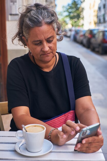 Enfoque superficial vertical de una mujer con su teléfono en la mesa exterior de un café