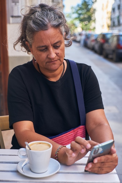 Enfoque superficial vertical de una mujer con su teléfono en la mesa exterior de un café