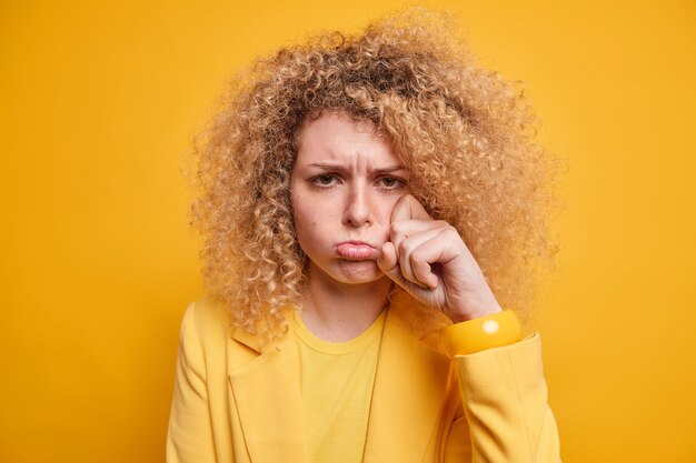 Enfurruñada mujer llorando ha deprimido mal humor enjuga lágrimas se queja de la vida difícil lloriquea con expresión molesta viste ropa elegante aislada sobre pared amarilla. Concepto de emociones negativas