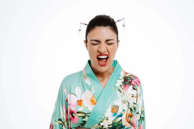 Foto gratuita enojado joven geisha en kimono japonés tradicional gritando con expresión molesta volviéndose salvaje de pie sobre la pared blanca