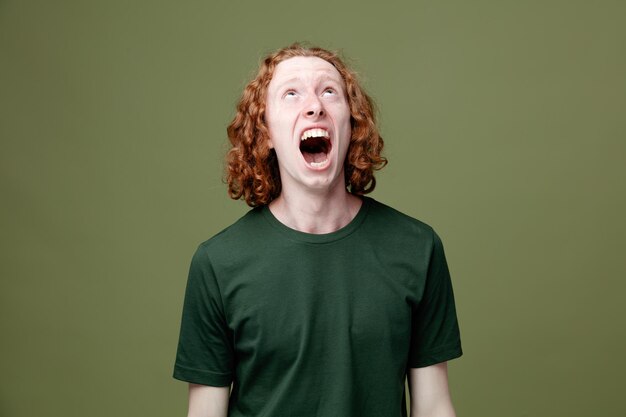 Enojado mirando a un joven apuesto que usa una camiseta verde aislado en un fondo verde