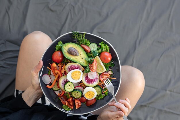 Ensalada apetitosa con verduras frescas y huevos en un plato en manos femeninas