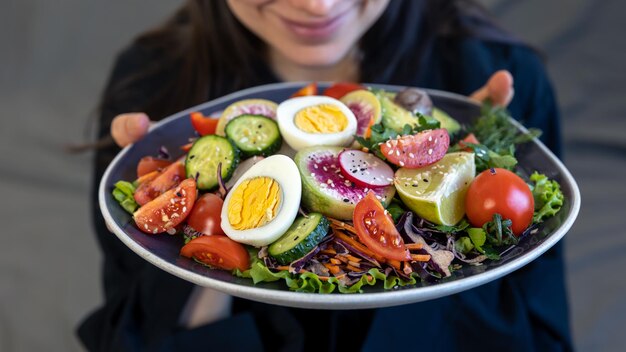 Ensalada apetitosa con verduras frescas y huevos en un plato en manos femeninas