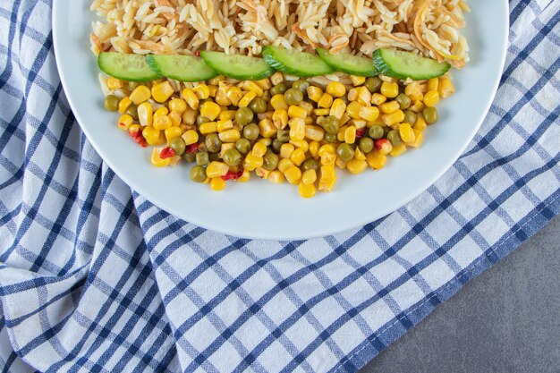 Ensalada de arroz y maíz en un plato sobre un paño de cocina, sobre la superficie de mármol.