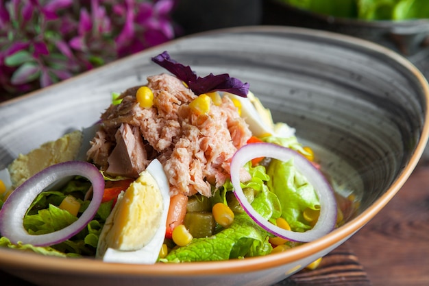 Ensalada de atún de primer plano con lechuga, huevos, tomates, pepino, cebolla y maíz en una mesa de madera oscura horizontal