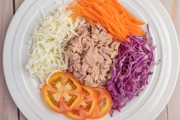 Ensalada de atún con zanahorias, tomates, repollo en un plato blanco sobre un piso de madera.