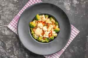 Foto gratuita ensalada de brócoli y coliflor de vista superior en plato ovalado negro en bandeja de servicio gris mantel a cuadros rosa y blanco sobre superficie oscura