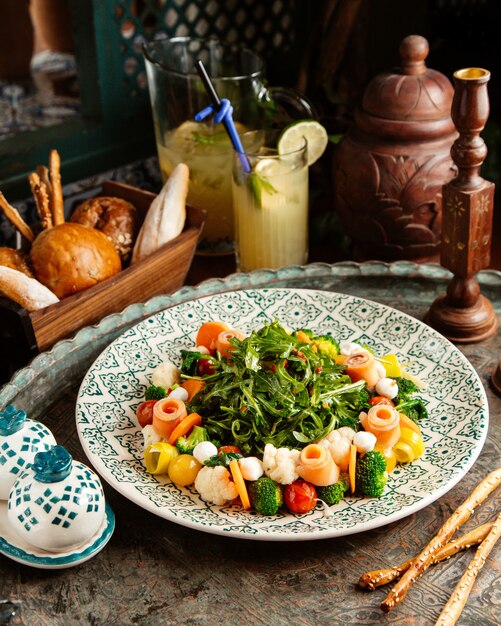 ensalada de brócoli con salmón carot coliflor mozzarellcherry tomates arugul limonada casera y pan en la mesa