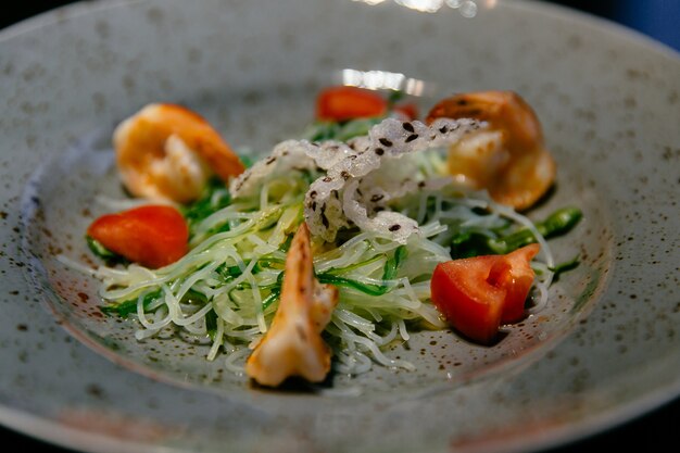 Ensalada de camarones, tomates y fideos de arroz, calabacín en plato blanco.