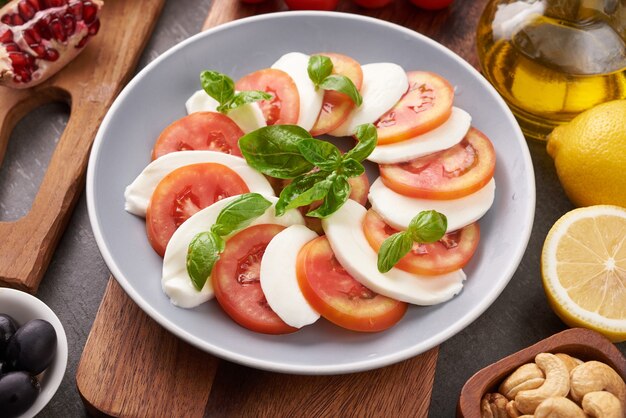 Ensalada Caprese italiana con tomate, albahaca, mozzarella, aceitunas y aceite de oliva sobre tabla de madera. Ingredientes de la ensalada caprese tradicional italiana. Concepto de comida mediterránea, orgánica y natural.