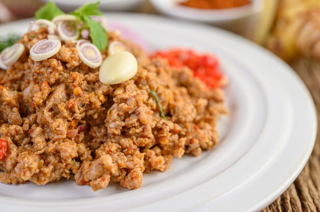 Ensalada de carne de cerdo picada picante en un plato blanco sobre mesa de madera.